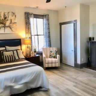 A cozy bedroom with modern decor, featuring a bed, an armchair, and a nightstand with a lamp.