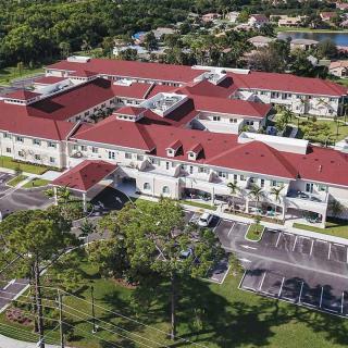 Aerial view of a large building with a red roof surrounded by greenery and parking areas.