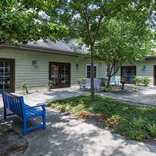 A serene courtyard featuring a blue bench, surrounded by trees and patio area.