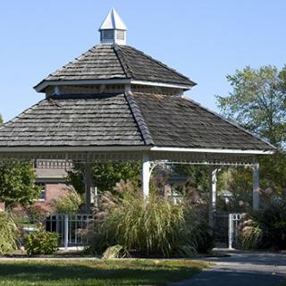 A charming gazebo surrounded by lush greenery and plants on a sunny day.