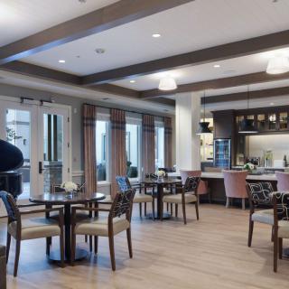 A modern restaurant interior with neatly arranged tables and chairs, featuring warm lighting and wood flooring.