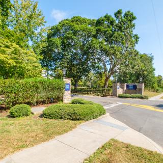 Entrance to a park area with lush greenery and a sidewalk.