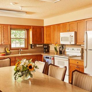 A cozy kitchen and dining area with wooden cabinets, modern appliances, and a centerpiece of flowers on the table.