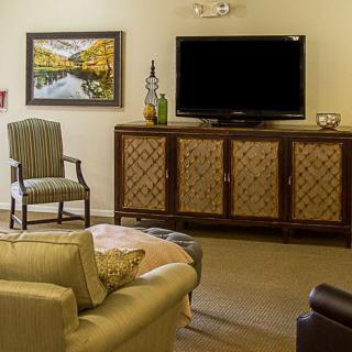 A cozy living room featuring a TV on a wooden cabinet, a comfortable sofa, and a decorative chair with a painting on the wall.