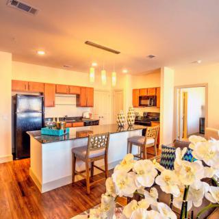A modern open-concept kitchen with a central island and dining area, featuring warm wood flooring and bright lighting.