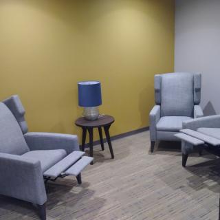 A modern living room setup with grey chairs, a blue lamp, and a yellow accent wall.
