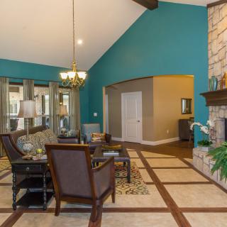 A spacious living room featuring a vaulted ceiling, blue accent wall, and a fireplace, with elegant furniture and a chandelier.