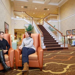 Two people conversing in a hotel lobby with a grand staircase in the background.