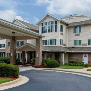 A residential building with a driveway and well-maintained landscaping under a cloudy sky.