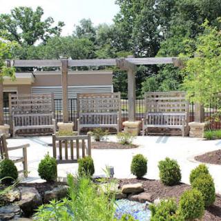A beautifully landscaped garden with benches and a pergola, surrounded by lush greenery.