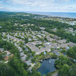 Aerial view of a residential neighborhood with houses, surrounded by greenery and a nearby lake, leading to a distant coastline.