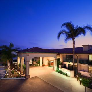 A modern building entrance illuminated at dusk, framed by palm trees.