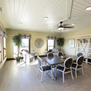 A bright dining room with a round table, six chairs, large windows, and decorative plants.