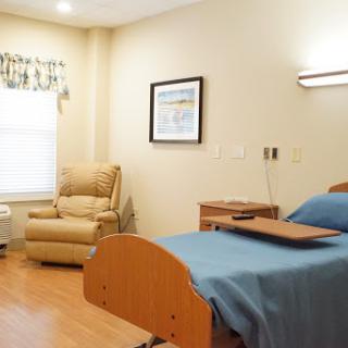 A comfortable hospital room featuring a bed, recliner, and warm lighting.