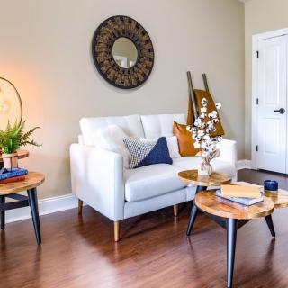 A modern living room with a white sofa, wooden coffee tables, a decorative mirror, and a potted plant.