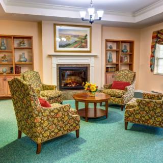 Cozy living room with armchairs arranged around a fireplace, decorated with shelves and artwork.