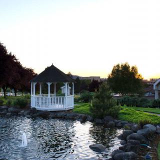 A peaceful garden scene featuring a white gazebo by a pond at sunset.