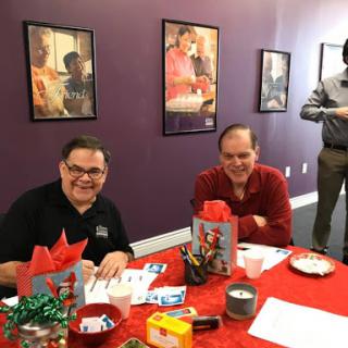 A cheerful gathering at a table adorned for a holiday event, featuring smiling attendees amidst festive decor.