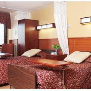 A hospital room with two beds separated by a curtain and wooden furniture.