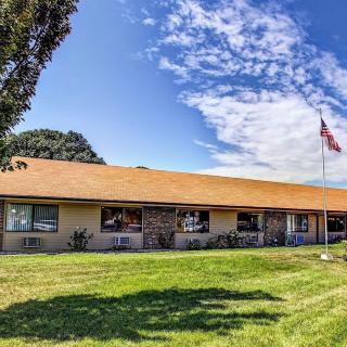 A single-story building with a sloping roof, surrounded by a lawn and an American flag waving under a partly cloudy sky.