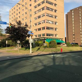 A view of a multi-story building at the intersection, surrounded by greenery and city life.