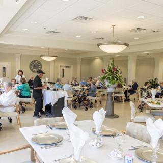 A spacious dining area with seniors seated at tables, and staff attending to them.