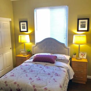 A cozy bedroom with a single bed, adorned with floral bedding. Two nightstands with lamps flank the bed, and a window provides natural light.