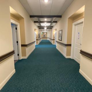 A long, well-lit hallway with doors on either side and a blue carpet.
