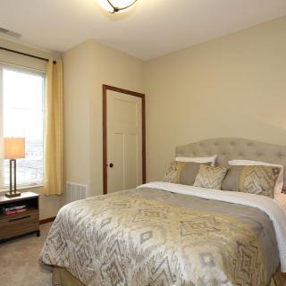 Cozy bedroom with a comfortable bed, bedside lamp, and natural light from the window.