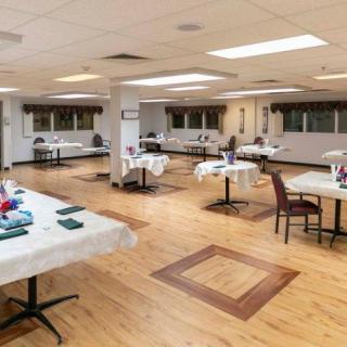 An empty banquet hall with arranged tables and chairs on a wooden floor.