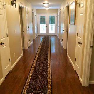 A well-lit hallway with wooden floors, featuring a long rug and doors on both sides.