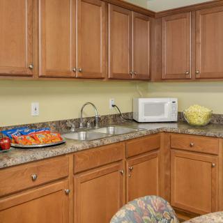 A kitchen with wooden cabinets, granite countertops, a microwave, and snacks on the counter.