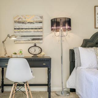 A cozy bedroom corner with a desk, chair, and floor lamp next to a bed.