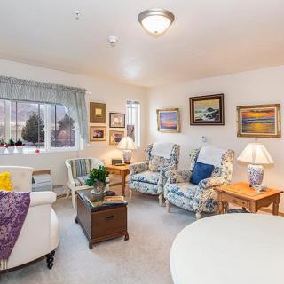 A cozy living room with floral-patterned armchairs, various artworks on the walls, and soft lighting from table lamps.
