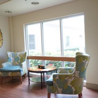 A cozy corner with patterned chairs and a small table, illuminated by natural light from the large windows.