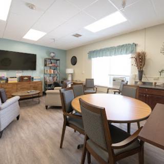 A cozy and well-lit meeting room featuring comfortable seating, tables for discussion, and a large television.