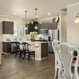 A modern kitchen with a dining area, featuring dark cabinets, stainless steel appliances, and pendant lighting.