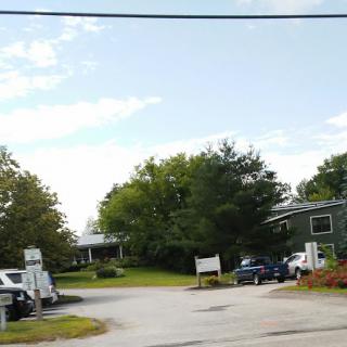 A view of a parking area surrounded by trees and buildings under a partly cloudy sky.