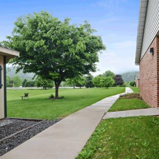 A scenic outdoor view featuring a walkway between buildings, with lush green grass and trees.