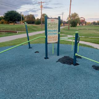 An outdoor fitness area equipped with exercise poles and rubberized flooring in a park.
