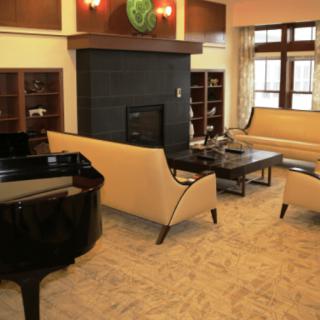 A cozy living room featuring a grand piano, modern furniture, and a central fireplace.