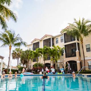 A lively apartment complex pool area with people enjoying the sun and water.