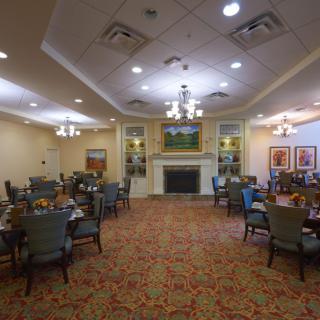 Elegant dining room with multiple tables and chairs, featuring a fireplace and chandeliers.