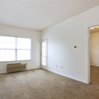 An empty room with carpeted floors, white walls, a window, and an air conditioning unit.