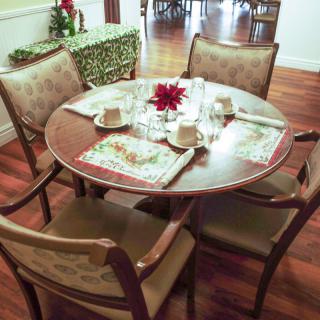 A dining table set for four with festive placemats and a floral centerpiece.