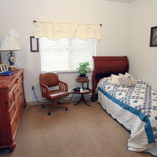 A cozy bedroom featuring a wooden bed, chair, and dresser with a quilted bedspread and a window with curtains.