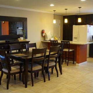 A modern dining and kitchen area with a wooden table, chairs, and pendant lighting.