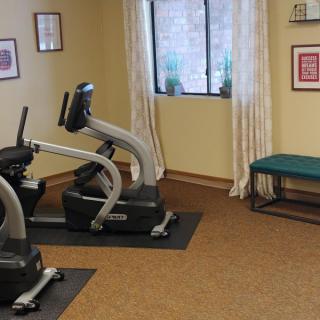 A small exercise room featuring stationary bikes and a bench, with wall art and a window providing natural light.