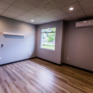 An empty room with hardwood flooring, ceiling lights, and an air conditioner.