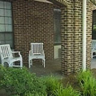 A brick porch with white plastic chairs and surrounding greenery.
